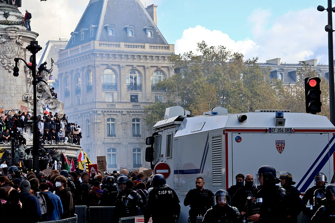 A crowd beside the République monument, riot police and a police water-cannon vehicle.