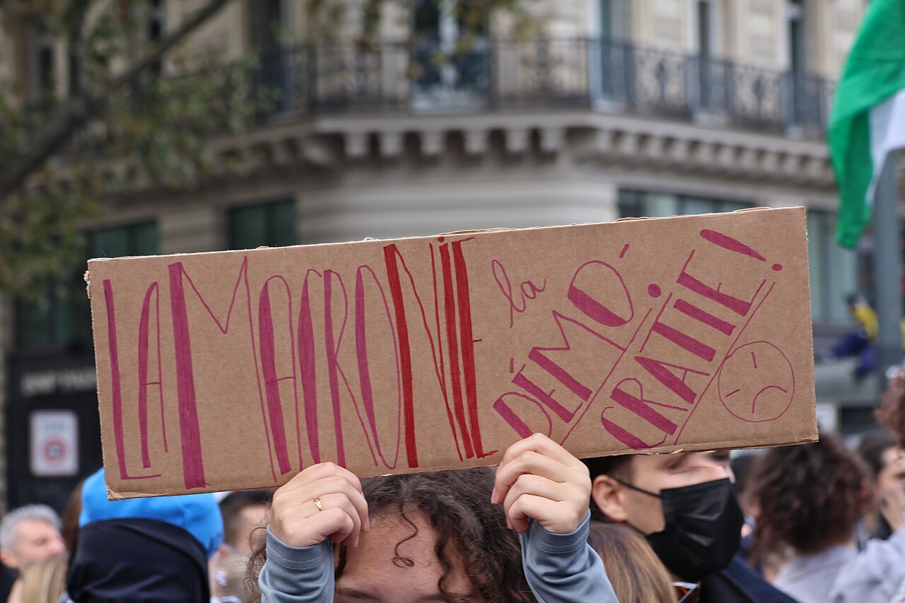 A participant holding a handwritten cardboard placard above a crowd.